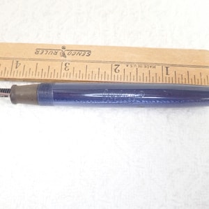 May include: A vintage blue fountain pen with a silver nib and a brown grip. A wooden ruler with inch markings is next to the pen. The pen is approximately 5 inches long.