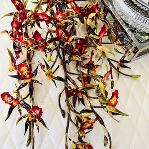 May include: A bouquet of artificial orchid stems with brown branches and red, yellow, and black spotted flowers.