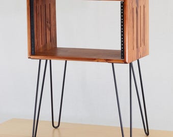 Puede incluir: Un mueble de audio de madera con un acabado marrón cálido, con un diseño de armario rectangular. El mueble tiene patas de horquilla de metal negro y listones verticales en los laterales. Diseñado para equipos de audio.