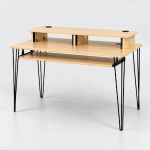 Op de afbeelding: Een bureau van licht hout met een verhoogde monitorplank voorzien van twee ronde kabeldoorvoeren, een uitschuifbare toetsenbordlade en vier dunne zwarte metalen haarspeldpoten. Het bureaublad is rechthoekig met een gladde afwerking.