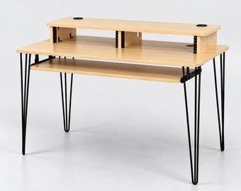 May include: A light wood desk featuring a raised monitor shelf with two circular cable management grommets, a sliding keyboard tray, and four thin black metal hairpin legs. The desk surface is rectangular with a smooth, light-coloured finish.