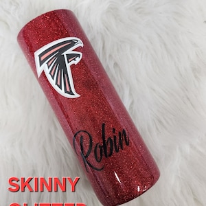 May include: A red glitter skinny tumbler with the name "Robin" in black script. The Atlanta Falcons logo is displayed in white and black. The words "SKINNY GLITTER" are in red.
