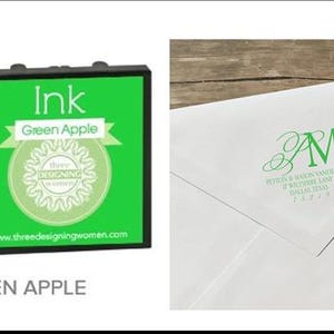 May include: Green apple ink pad with a matching green ink drop graphic. The ink pad is black with a green label that reads "Ink Green Apple" and features a logo. A white envelope with green initials and address is shown with pens.