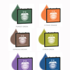 May include: Image of ink stamp pads in various colors, including Forest Green, Citrine Orange, Espresso Brown, Citron Green, Passion Purple, and Newport Navy. Each pad is square with a black frame and a label indicating the ink color.