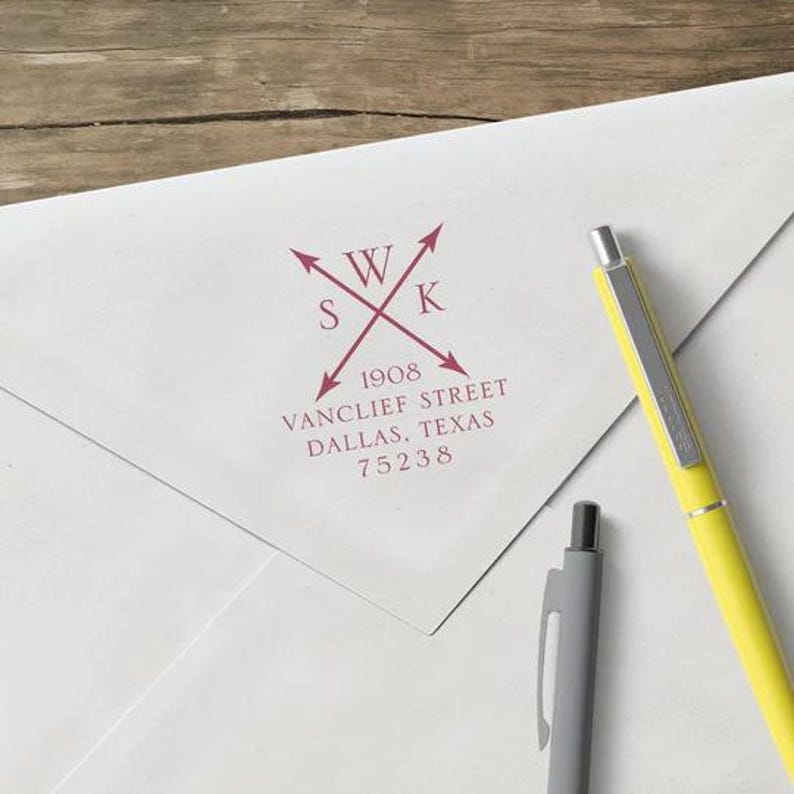 May include: A white envelope with a burgundy address stamp. The stamp features the initials "WKS" crossed with arrows, along with the address: 1908 Vanclief Street, Dallas, Texas 75238. A yellow pen and a gray pen are also in the image.