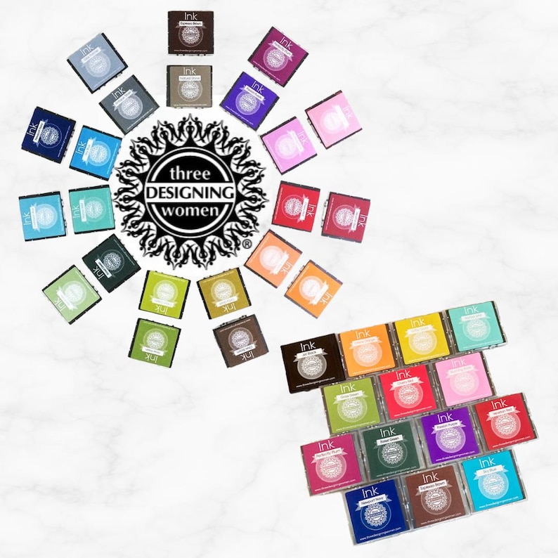 May include: An overhead shot displays a collection of ink pads in various colors, arranged in a circular pattern around a central logo that reads "three DESIGNING women." Each pad is labeled "Ink."