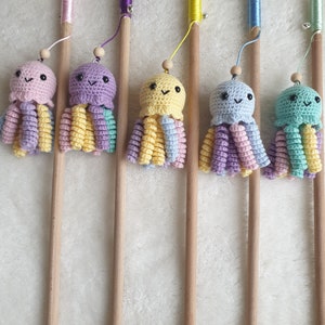 Op de afbeelding: Zes kleurrijke gehaakte octopus speelgoedjes bevestigd aan houten stokken met touw. De octopus speelgoedjes zijn in tinten roze, paars, geel en blauw.