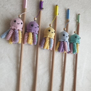 Op de afbeelding: Zes kleurrijke gehaakte octopus speelgoedjes bevestigd aan houten stokken. Elke octopus heeft een andere kleurencombinatie, waaronder roze, geel, blauw en groen. De stokken hebben een touw aan de bovenkant.