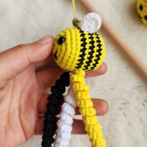 Pu&ograve; includere: Un giocattolo a forma di ape realizzato a uncinetto con strisce gialle e nere, ali bianche e gambe pendenti nere, bianche e gialle.
