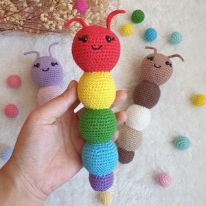May include: Three crocheted caterpillar toys. The first is red, yellow, green, blue, and purple. The second is purple and the third is brown. Each caterpillar has a smiling face with black eyes and a black mouth.