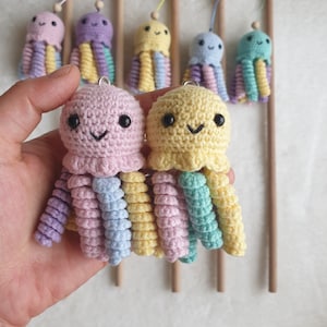 Op de afbeelding: Twee gehaakte octopus speelgoedjes met lachende gezichten. De octopus links is roze met paarse, lichtblauwe en gele tentakels. De octopus rechts is geel met groene, lichtblauwe en gele tentakels.