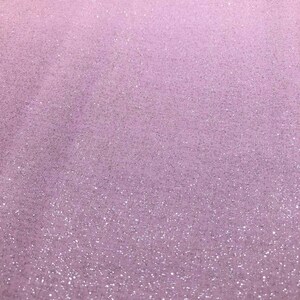 May include: A close-up of a light purple fabric with a subtle glitter effect. The fabric has a soft, textured appearance, and the glitter is scattered across the surface, creating a shimmering effect. The overall look is delicate and elegant.