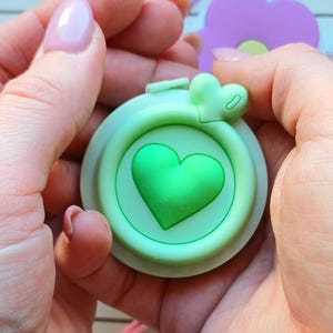 May include: A green silicone food container lid with a heart-shaped design. The lid has a small heart-shaped handle on the top.
