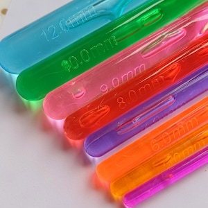 Pu&ograve; includere: Un set di sei ferri da maglia in plastica colorati, che vanno da 6,0 mm a 12,0 mm. I ferri sono disposti a forma di arcobaleno, con il ferro pi&ugrave; grande in alto e il pi&ugrave; piccolo in basso.