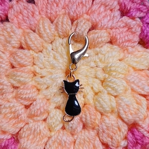 Black cat themed stitch marker with gold clasp and black and gold enamel cat charm, displayed as attached to colourful crochet fabric—cute and functional stitch marker accessories for knitting and crochet projects.