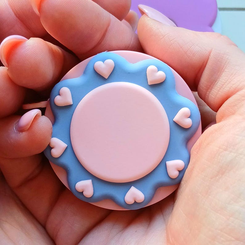 May include: A blue and pink heart-shaped measuring tape with a white background. The tape is held in a hand.