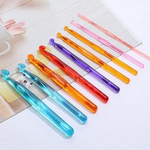 Pu&ograve; includere: Un set di 10 uncinetti di plastica colorati. Gli uncinetti sono disposti in una fila dal pi&ugrave; piccolo al pi&ugrave; grande, con l'uncinetto pi&ugrave; piccolo di colore rosa chiaro e l'uncinetto pi&ugrave; grande di colore blu chiaro.