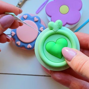 May include: A set of three colorful retractable tape measures shaped like flowers. Each tape measure has a different color and design. The tape measures are made of plastic and have a metal hook at the end.