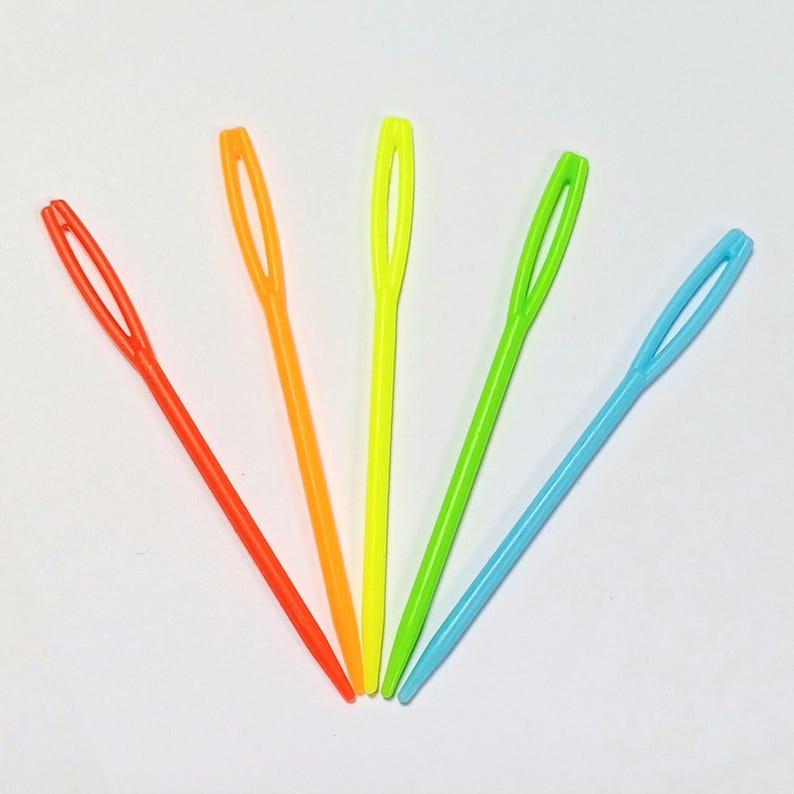 K&ouml;nnte beinhalten: F&uuml;nf bunte Plastik-Garnnadeln, in F&auml;cherform angeordnet. Die Nadeln sind orange, gelb, gr&uuml;n, hellblau und blau.