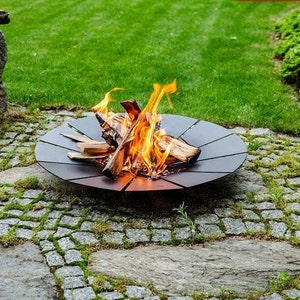 May include: A round, black metal fire pit with a decorative design sits on a stone patio. A small fire burns inside the pit with flames and glowing embers.