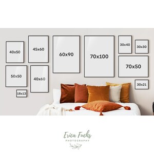 May include: A collection of black framed prints of various sizes hanging on a wall above a bed with orange and brown throw pillows. The prints are labeled with their dimensions in inches, such as 40x50, 60x90, and 70x100.