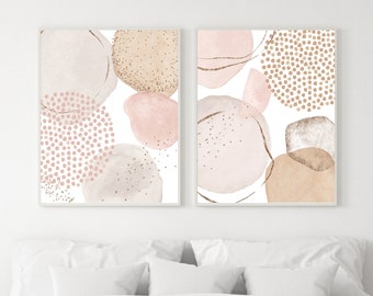May include: Two abstract art prints with pink, brown, and gold watercolor shapes. The prints are framed in white and are hanging on a white wall above a white bed with a white blanket.