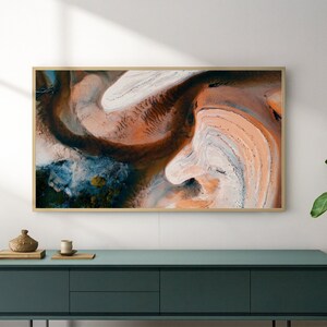 May include: A framed abstract art print with swirling patterns in shades of brown, orange, white, and blue. The print is hanging on a white wall above a teal blue dresser.