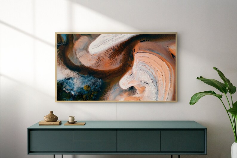 May include: A framed abstract art print with swirling patterns in shades of brown, orange, white, and blue. The print is hanging on a white wall above a teal blue dresser.
