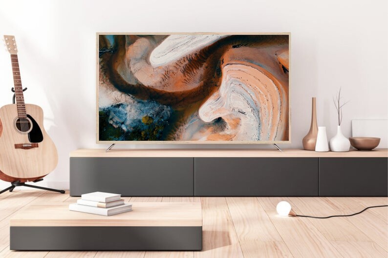 May include: A modern living room interior with a flat screen TV on a dark grey entertainment center. The TV is displaying an abstract image of swirling colors. There are decorative vases and a lamp on the shelf above the entertainment center.