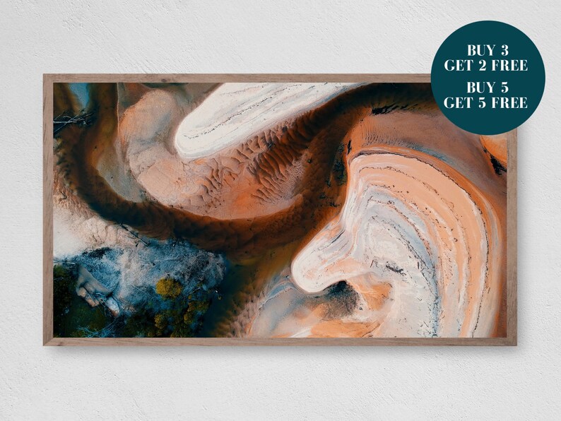 May include: An abstract aerial photograph of a landscape with swirling patterns of orange, brown, white, and blue. The image is framed in a wooden frame.
