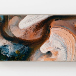 May include: Abstract aerial photograph of a landscape with swirling patterns of orange, brown, white, and blue. The image is framed in a light wood frame.