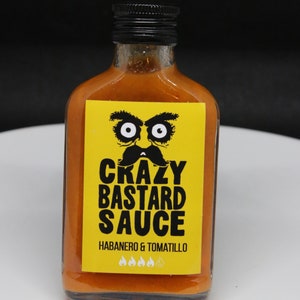 May include: A yellow bottle of hot sauce with a black label that says "Crazy Bastard Sauce" with a cartoon face and the words "Habanero & Tomatillo" and four flames.
