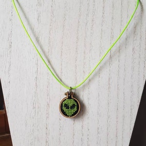 Alien head mini cross stitch necklace - completed on a mini hoop and hung on green cord