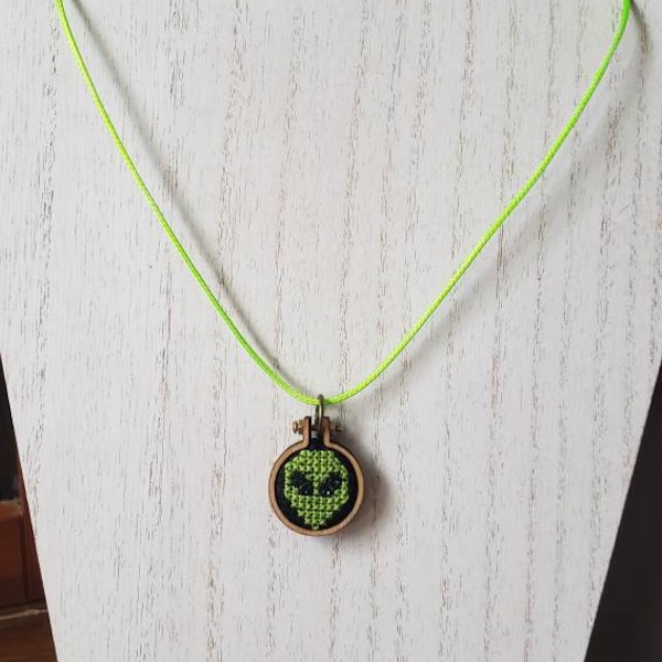 Mini collar de punto de cruz con cabeza de alienígena - completado en un mini aro y colgado de un cordón verde