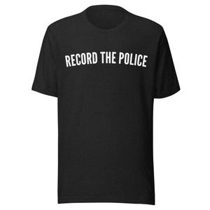 Puede incluir: Camiseta negra con el texto blanco "RECORD THE POLICE" en una fuente curva. La camiseta tiene cuello redondo y mangas cortas. La tela parece suave y cómoda.