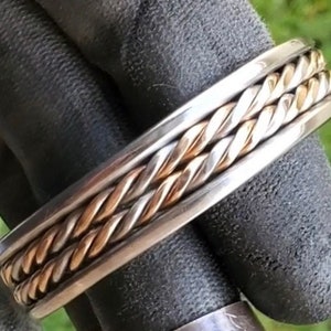 May include: A silver and gold braided bracelet with a twisted design.