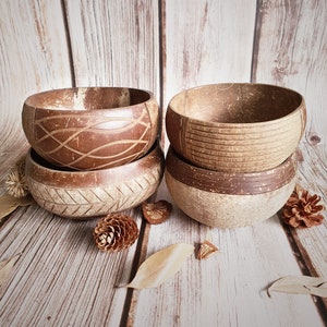 May include: Four brown coconut bowls stacked on top of each other. The bowls have different patterns carved into them. The bowls are sitting on a wooden surface.