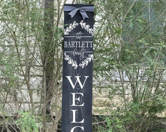 May include: Black wooden welcome sign with white lettering that reads "WELCOME" and a wreath with the text "The Bartlett Family".