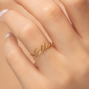 May include: A gold-colored ring with the word "Ella" written in cursive script.