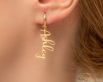 May include: Gold dangle earrings with the name "Ashley" written in cursive.