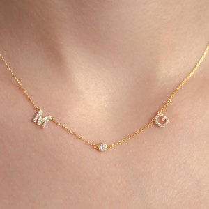 May include: A gold chain necklace with two initial charms, an "M" and a "G", and a small diamond charm in the center.