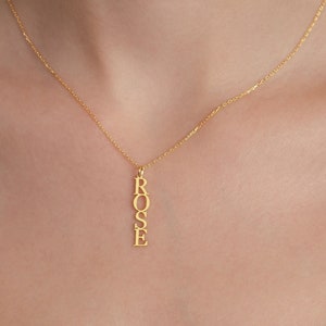 May include: A gold chain necklace with a vertical pendant spelling out the name "ROSE".