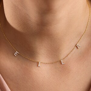 May include: A gold chain necklace with four small, dangling letters that spell "ELLI" in diamonds.