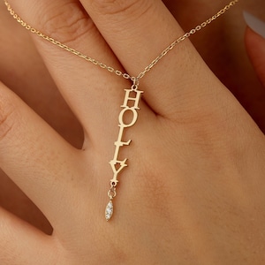 May include: A gold necklace with a vertical name pendant that reads "HOLLY" with a small diamond dangle at the bottom.