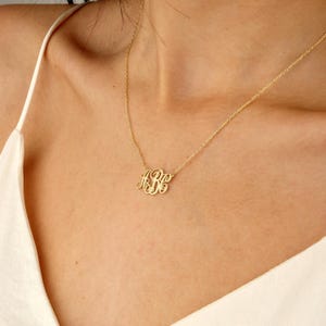 May include: A gold-colored monogram necklace with the letters "ABC" in a delicate, cursive font. The necklace is displayed on a person's chest, showcasing the pendant's design and the chain's subtle elegance. The necklace is a personalized jewelry item.