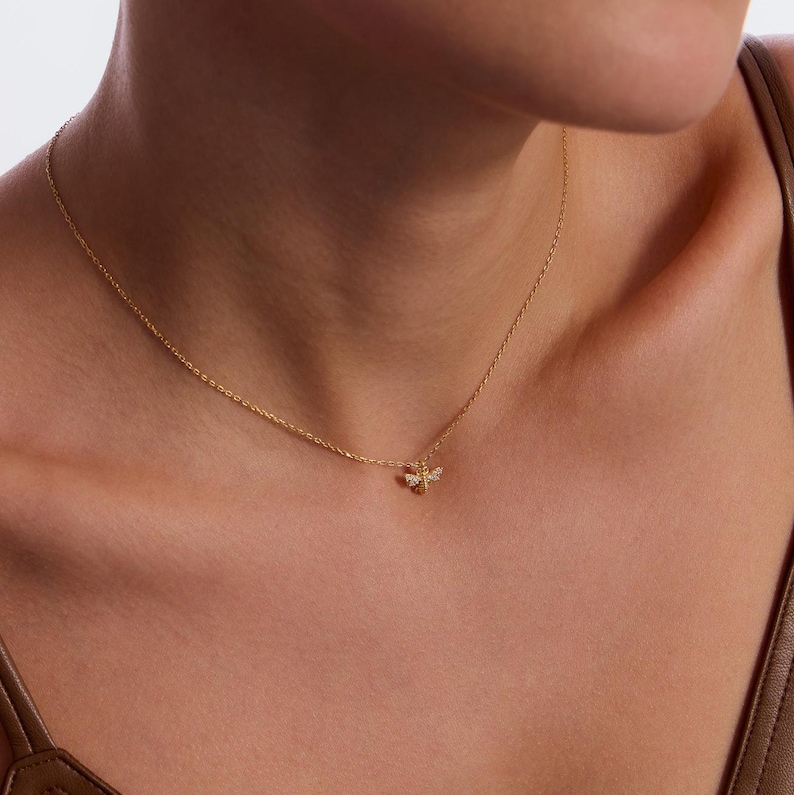 May include: A gold chain necklace with a small bee pendant adorned with tiny clear stones.