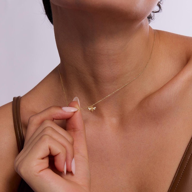 May include: A gold chain necklace with a small bee pendant featuring clear cubic zirconia stones.