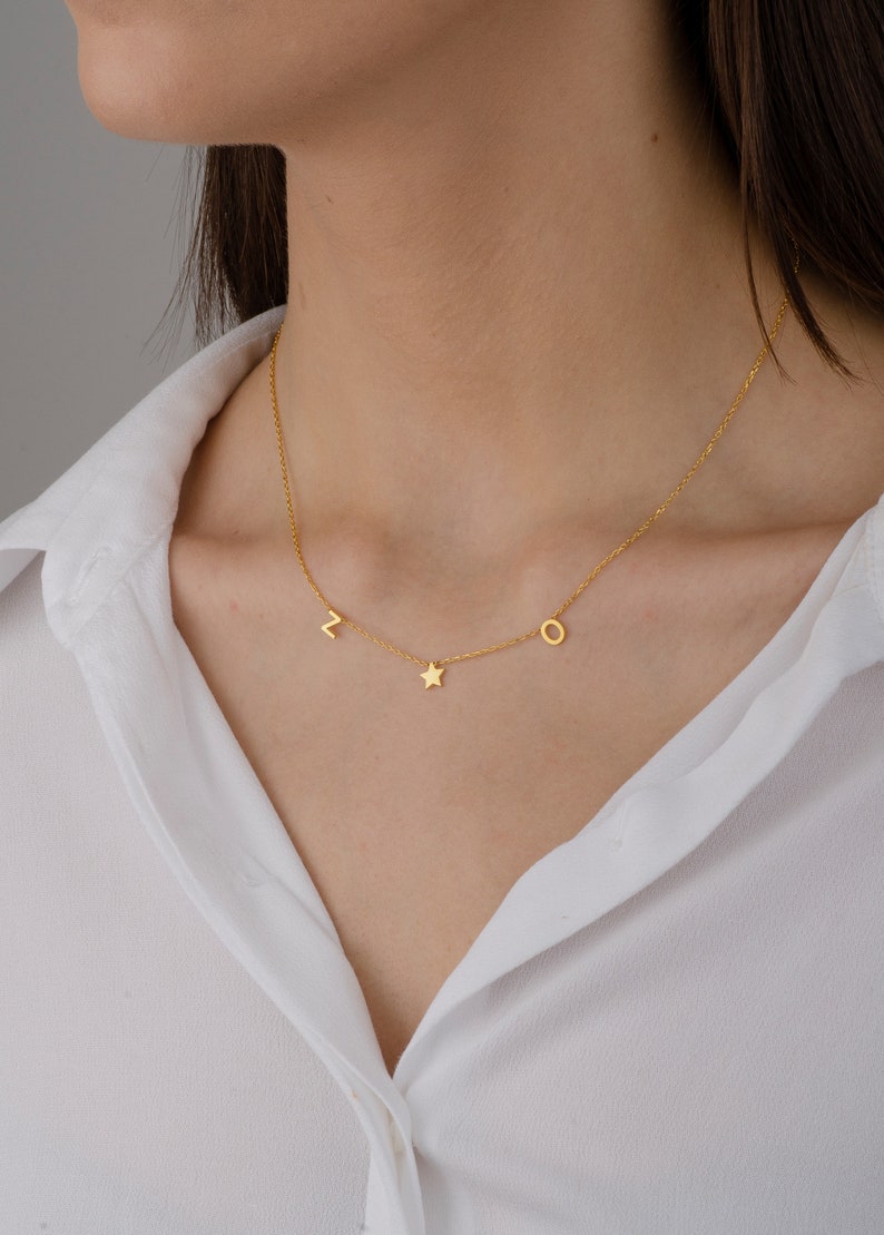 May include: A gold chain necklace with a star charm and letter charms "L" and "O".