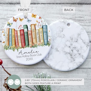 May include: A round porcelain ornament, 2.85 inches (73mm), with a front design featuring a stack of colorful books, butterflies, and flowers. The back has a white marble pattern. Text includes "Amelie", "Stars Hollow Book Club", and "20XX".