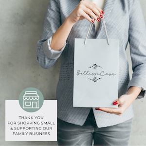 May include: A person holding a white shopping bag with the text "Bellissima Casa" and a floral design. The bag has a green and white store icon and the text "Thank you for shopping small & supporting our family business".